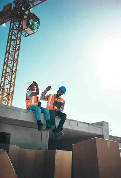 Quand ton bureau se sent comme une aire de jeux. Prise de vue d'un jeune homme et d'une jeune femme assis au sommet d'un bâtiment sur un chantier de construction et se donnant un haut cinq. — Photo