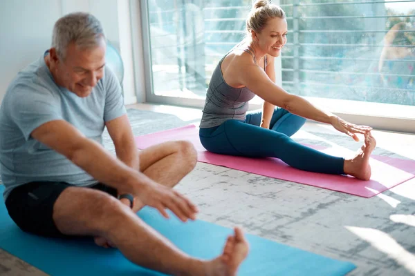 Att få in en bra uppvärmning. Hög vinkel skott av ett moget par sträcker sig på yogamatta innan du tränar hemma. — Stockfoto