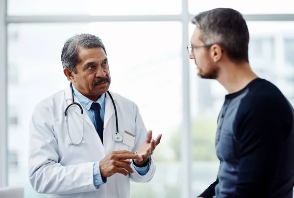 Hij legt uit welke stappen er genomen moeten worden. Shot van een zelfverzekerde volwassen mannelijke arts raadplegen van een patiënt in een hospit. — Stockfoto