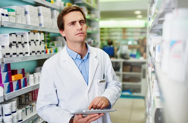 Digitalização de tarefas de gestão de farmácias. Tiro de um jovem farmacêutico usando um comprimido digital em uma farmácia. — Fotografia de Stock