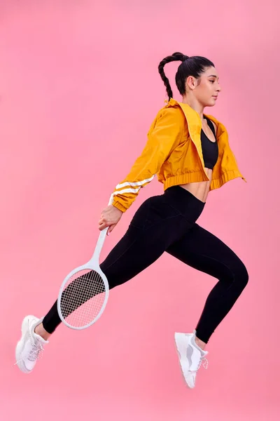Volají tenisové kurty a já musím jít. Studio záběr sportovní mladé ženy skákání s tenisovou raketou na růžovém pozadí. — Stock fotografie