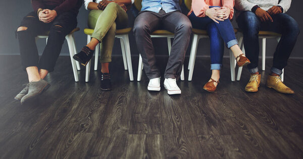 Good things come to those who wait. Cropped studio shot of a group of people waiting in line on chairs against a gray background.