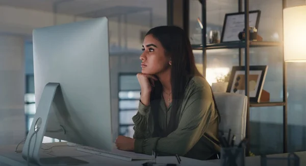 Je cherche un peu plus d'inspiration. Prise de vue d'une jeune femme d'affaires regardant réfléchie tout en travaillant sur un ordinateur dans un bureau la nuit. — Photo