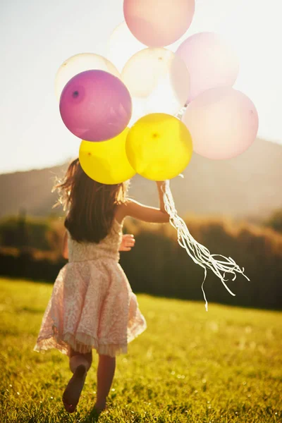 Jolies couleurs dans le vent. Vue arrière d'une petite fille non identifiable tenant un gros tas de ballons tout en marchant à l'extérieur. — Photo