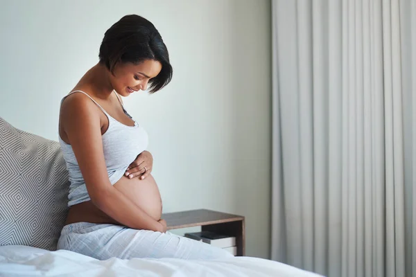 Non vedo l'ora di viziarti con tutto il mio amore. Girato di una giovane donna felice incinta seduta su un letto e tenendo la pancia nella sua camera da letto a casa. — Foto Stock