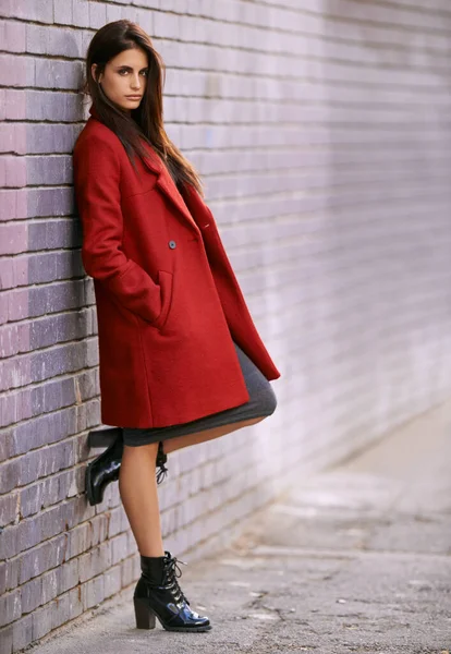 Winter ready in red. Portrait of a gorgeous young woman leaning against a brick wall in the city. — Stock Photo, Image