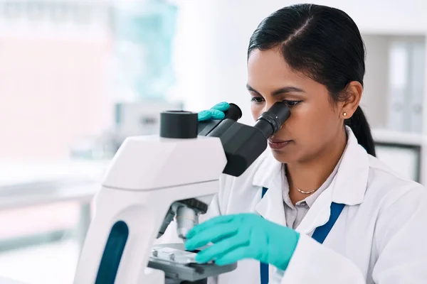 Jedno spojrzenie dzieli ją od dokonania odkrycia. Przycięte ujęcie atrakcyjnej młodej kobiety naukowca patrzącej przez mikroskop podczas pracy w laboratorium. — Zdjęcie stockowe