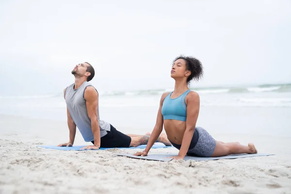 Дозвольте всім почуттям відчувати спокій. Знімок молодого чоловіка і жінки, що практикує йогу разом на пляжі . — стокове фото