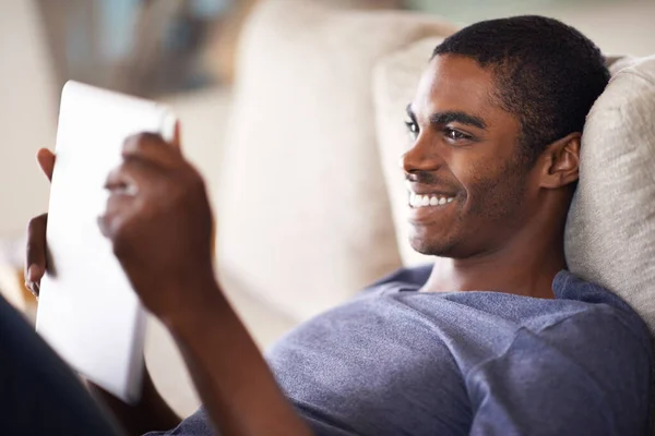 Genieten van wat downtime met zijn digitale tablet. Gehakt schot van een knappe jonge man met behulp van zijn tablet terwijl ontspannen thuis. — Stockfoto