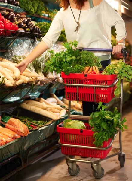 A abastecer-se de vegetais frescos. Imagem cortada de uma mulher empurrando um carrinho no supermercado. — Fotografia de Stock