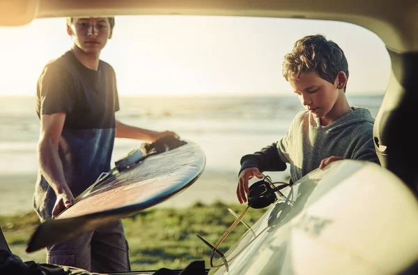 Surfeamos, por lo tanto lo somos. Disparo de dos hermanos jóvenes descargando sus tablas de surf desde la parte trasera de un coche en la playa. —  Fotos de Stock