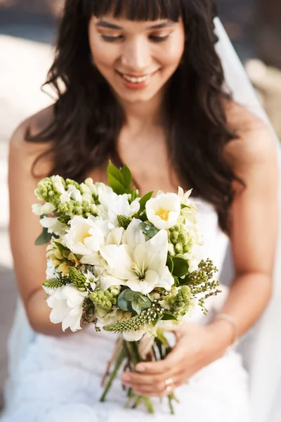 I feel as beautiful as these flowers are. Cropped shot of a beautiful young bride holding a bouquet of flowers while sitting outdoors on her wedding day. — Stock Photo, Image