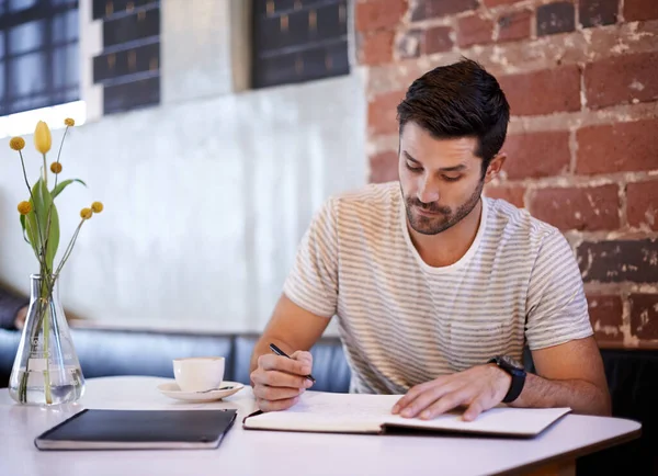 Las cosas de escribir. Fotografía de un joven guapo escribiendo en un cuaderno mientras estaba sentado en la mesa de un restaurante. — Foto de Stock