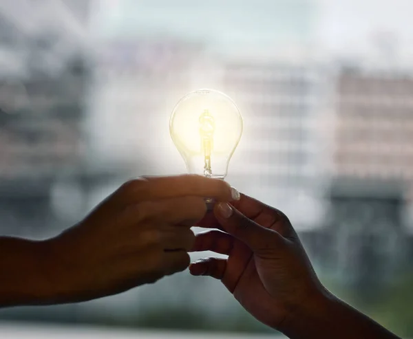 Idéer händer när lag samarbetar. Beskuren skott av två oigenkännliga företagare som står tillsammans och håller en glödlampa på kontoret. — Stockfoto