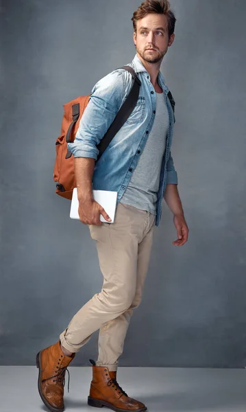 Er reist leicht. Aufnahme eines gutaussehenden jungen Mannes mit einem Rucksack, der ein Tablet hält, während er im Studio steht. — Stockfoto