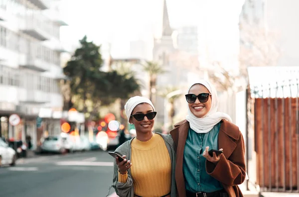 这是千年一代。两名年轻迷人的穆斯林女子戴着太阳镜，一边举着手机一边游览城市，拍了照. — 图库照片