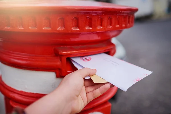 The old fashioned way of messaging. Closeup of an unrecognizable persons hand sliding in letters into a red mailbox outside during the day. — Stock Photo, Image