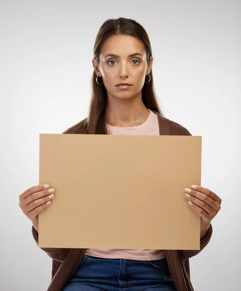 Das ist eine ernste Angelegenheit. Aufnahme einer jungen Frau mit einem leeren Schild vor grauem Hintergrund. — Stockfoto