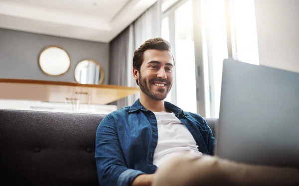 Há sempre coisas fixes para ver na internet. Tiro de um jovem bonito usando seu laptop enquanto relaxa em um sofá em casa. — Fotografia de Stock