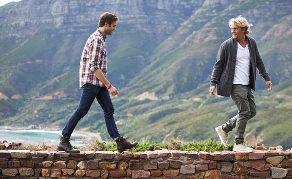 Bindung mit meinem Kumpel im Freien. Aufnahme von zwei jungen Männern, die auf einer Steinmauer gehen, mit dem Berg im Hintergrund. — Stockfoto