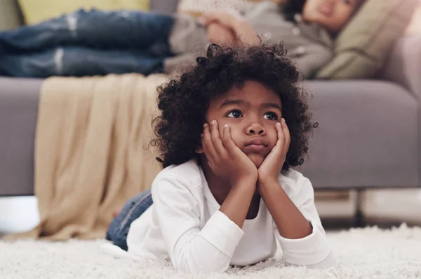 I wonder if therell be a part two. Shot of an adorable little boy lying down on a carpet and watching tv at home. — Stock Photo, Image