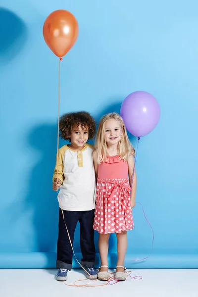 Είναι η παιδική μου αγάπη. Πορτρέτο ενός χαριτωμένο κοριτσάκι και αγόρι κρατώντας ένα μπαλόνι πάνω από ένα μπλε φόντο. — Φωτογραφία Αρχείου