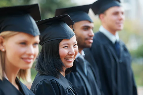 З нетерпінням чекаємо їхнього майбутнього. Молоді випускники коледжу тримають свої дипломи, стоячи підряд і посміхаючись . — стокове фото