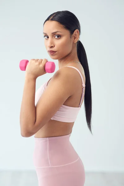 Cada vez más fuerte. Retrato recortado de una atractiva atleta joven posando con una mancuerna en el estudio sobre un fondo gris. — Foto de Stock