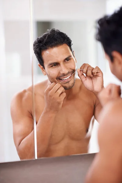 Es ist wichtig, jeden Tag Zahnseide zu tragen. Ein junger Mann mit Zahnseide, während er in den Spiegel schaut. — Stockfoto