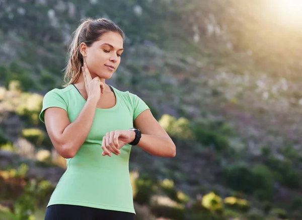 Se pone más en forma cada día. Fotografía de una joven que comprueba su ritmo cardíaco mientras hace ejercicio al aire libre. — Foto de Stock
