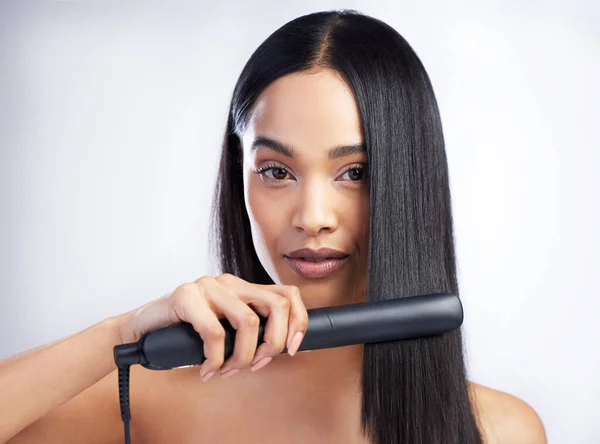 ¿Cómo consigo el pelo liso? Fotografía de una joven atractiva parada sola en el estudio y peinándose el pelo con una plancha de pelo. — Foto de Stock