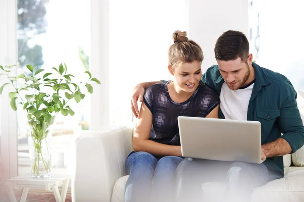 Ligado de várias maneiras. Tiro de um jovem casal feliz usando um laptop enquanto relaxam em casa juntos. — Fotografia de Stock