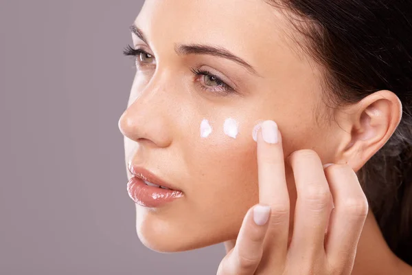 Dándole a su piel la hidratación que necesita. Foto de estudio de una hermosa joven que se aplica un producto para el cuidado de la piel en la cara. —  Fotos de Stock
