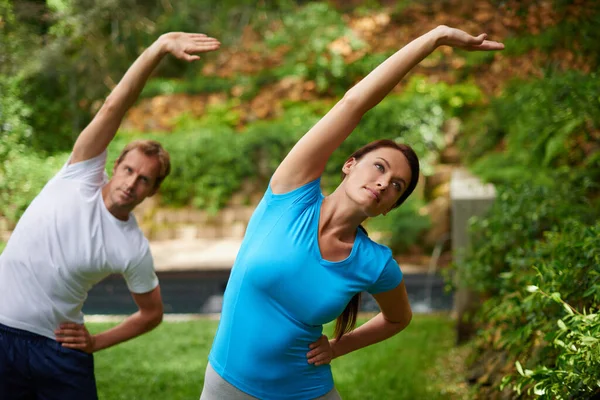 Vägen till flexibilitet. Skott av en man och kvinna som utför en sidosträcka i en yogaklass utomhus. — Stockfoto