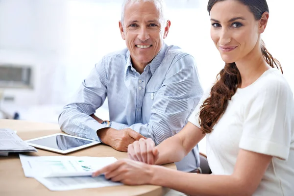 Fazer o trabalho com um sorriso. Tiro de dois colegas lendo papelada enquanto sentados em uma mesa em um escritório. — Fotografia de Stock