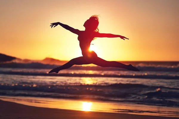 Corre un riesgo. Silueta de una mujer enérgica saltando en la playa al atardecer. —  Fotos de Stock