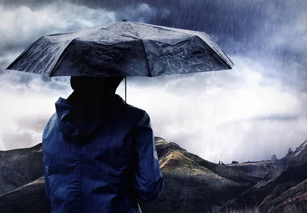 A storm is brewing. Shot of a woman covered with an umbrella watching a thunderstorm over a mountain. — Stock Photo, Image