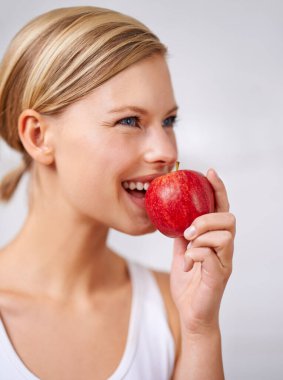 Çok taze ve lezzetli. Lezzetli bir kırmızı elma yiyen genç ve güzel bir kadının kırpılmış fotoğrafı..