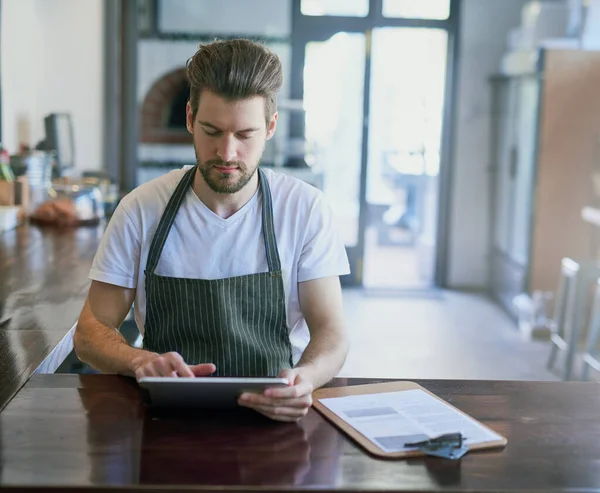 Everything at the touch of a button. Cropped shot of a young barista using a tablet in his coffee shop. — Stock Photo, Image