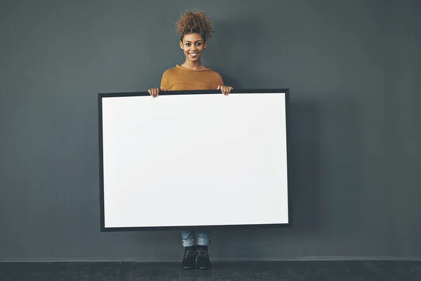 Ich werde Werbung für Ihre Nachricht machen. Studioporträt einer jungen Frau mit einem leeren Schild vor grauem Hintergrund. — Stockfoto