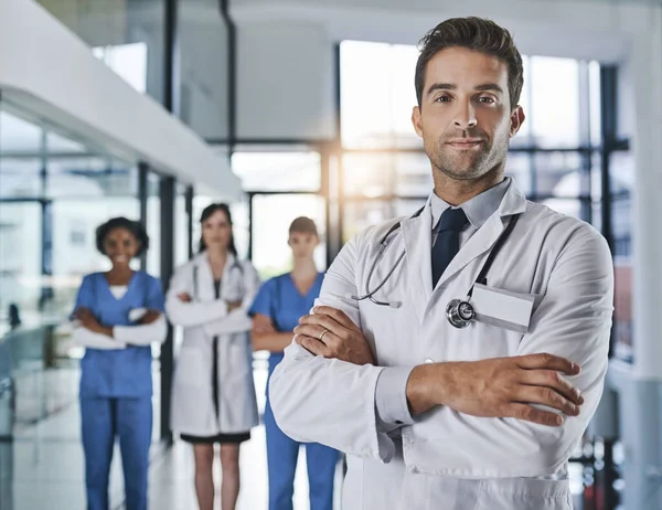 Dirigo un ospedale ad alte prestazioni. Ritratto di un giovane medico fiducioso che lavora in ospedale con i suoi colleghi sullo sfondo. — Foto Stock
