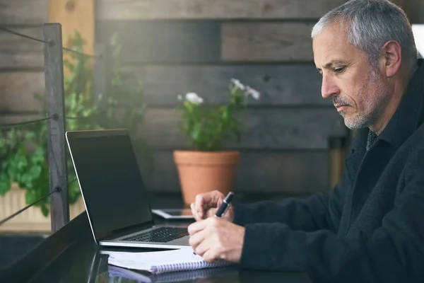Notizen machen. Aufnahme eines reifen Geschäftsmannes, der Notizen schreibt, während er seinen Laptop in einem Café benutzt. — Stockfoto
