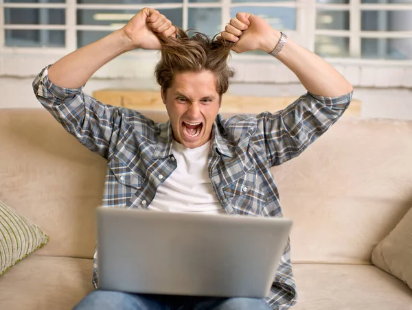 Quando a tecnologia falha, a raiva surge. Um jovem olhando frustrado enquanto trabalhava em seu laptop. — Fotografia de Stock
