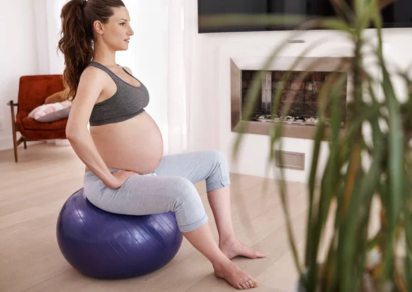 ती तिच्या गर्भधारणेद्वारे व्यायाम करते. घरी व्यायाम करणार्या एका तरुण गर्भवती महिलेचा शॉट . — स्टॉक फोटो, इमेज