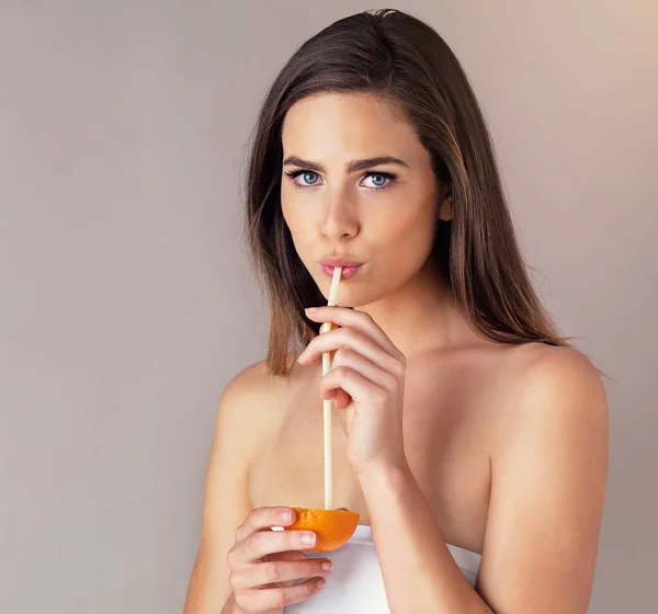 Bebendo um pouco de vitamina c. Estúdio retrato de uma jovem atraente bebendo de uma laranja contra um fundo roxo. — Fotografia de Stock