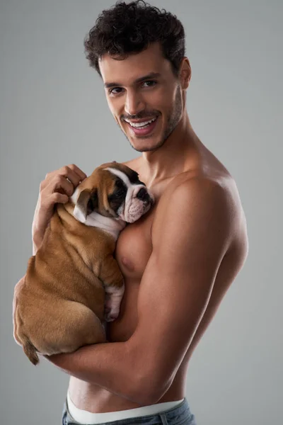 Es el paquete perfecto, guapo y cariñoso. Estudio de un joven guapo posando con su cachorro sobre un fondo gris. — Foto de Stock