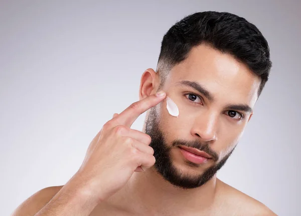 Diese Gesichtscreme spendet tiefe Feuchtigkeit. Aufnahme eines gut aussehenden jungen Mannes, der vor Studiohintergrund Feuchtigkeitscreme auf sein Gesicht aufträgt. — Stockfoto