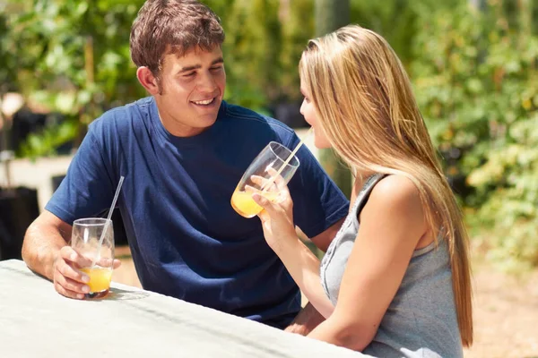 Disfrutando de una cita tranquila. Una joven pareja sentada afuera y bebiendo jugo de naranja. — Foto de Stock