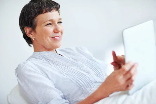 Donna matura che utilizza tablet PC a casa. Rilassato donna matura utilizzando tablet PC mentre seduto sul divano. — Foto Stock