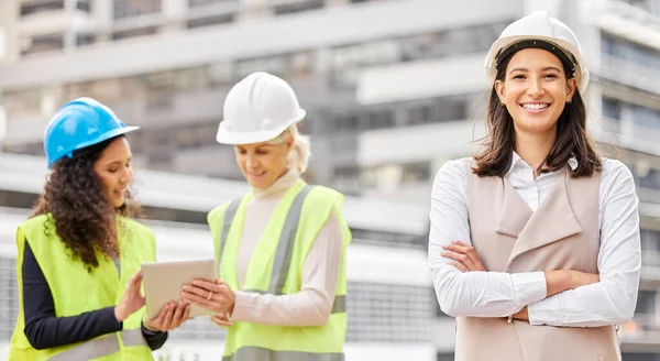 Ze hebben alles onder controle. Gesneden portret van een aantrekkelijke jonge vrouwelijke ingenieur met gevouwen armen met haar collega 's op de achtergrond op een bouwplaats. — Stockfoto